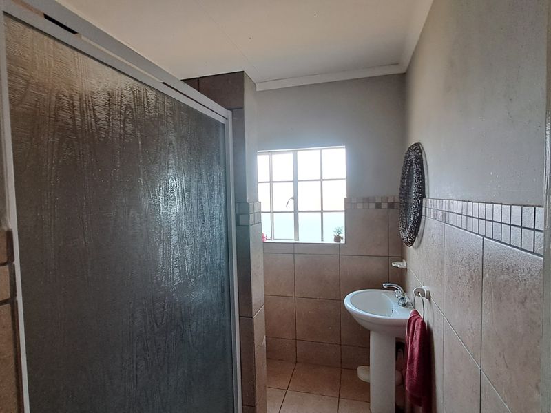 A functional bathroom featuring a pedestal basin, tiled walls, and a shower enclosure with a textured glass door.