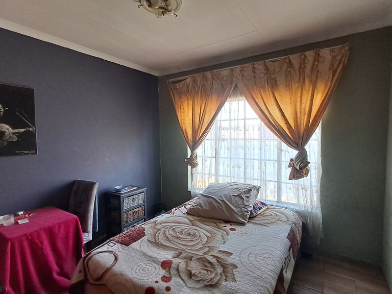 A bedroom featuring tiled flooring and a window fitted with security bars, requiring cosmetic updates to the wall finishes.