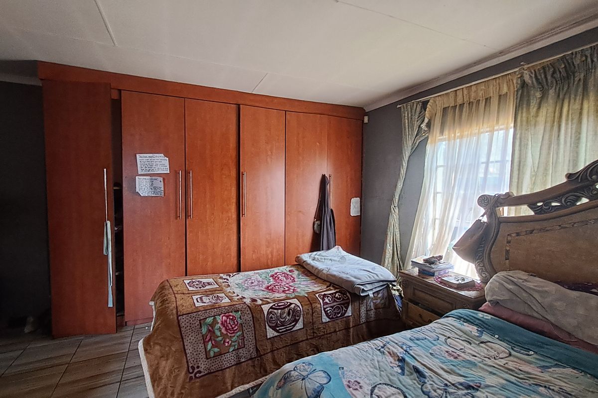 A bedroom featuring built-in wooden cupboards and tiled flooring, offering a functional space with potential for cosmetic updates to modernize the interior finishes.