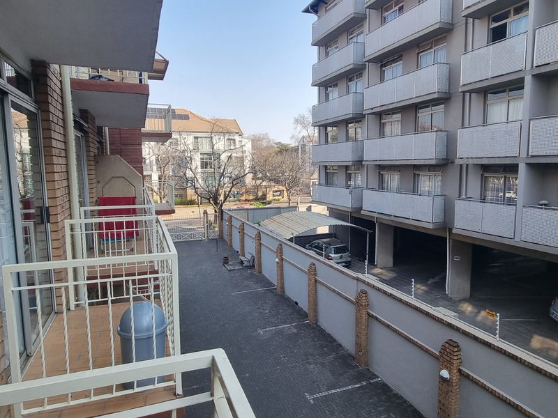 A view from a balcony overlooking a paved courtyard and parking area within an apartment complex, featuring metal railings and brick exterior finishes.