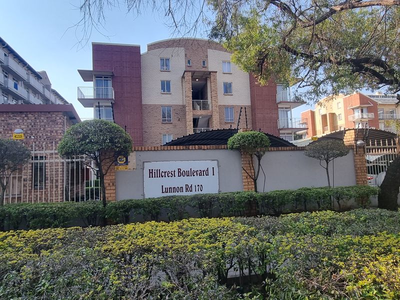 Street view of the Hillcrest Boulevard I apartment complex entrance, featuring a secure perimeter wall, electric fencing, and established garden landscaping.
