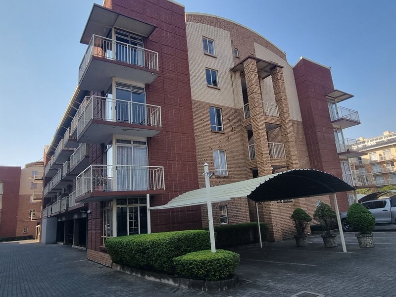 Exterior view of a multi-story apartment complex featuring brick facade, private balconies, and a paved parking area with covered carports.