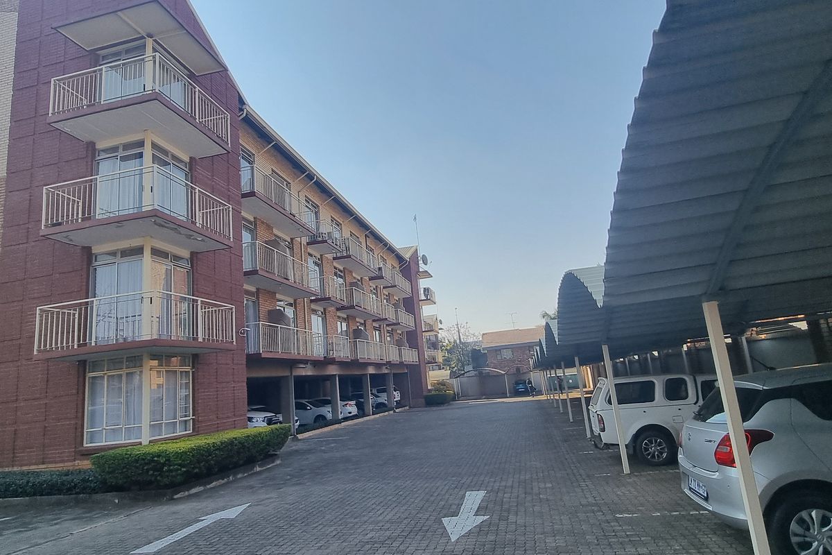 Exterior view of an apartment complex featuring a brick facade, multiple balconies, and a paved parking area with covered carports.