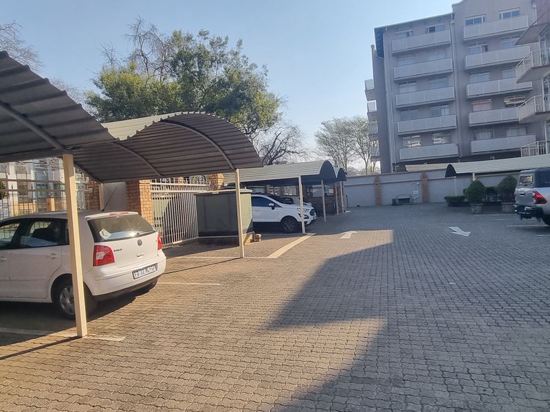 Outdoor parking area featuring covered carports, paved driveway, and secure perimeter fencing within an apartment complex setting.