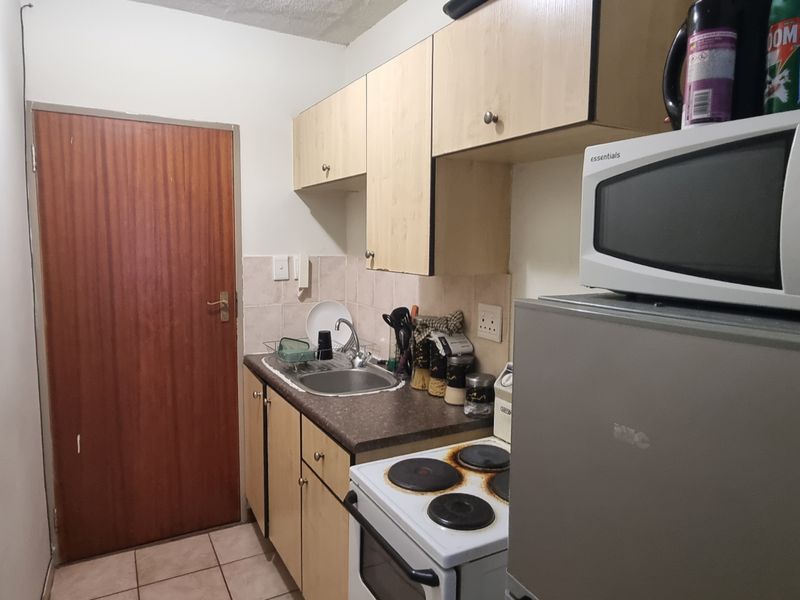 A compact kitchen featuring laminate cabinetry, a stainless steel sink, and an electric stove with tiled splashback and flooring.
