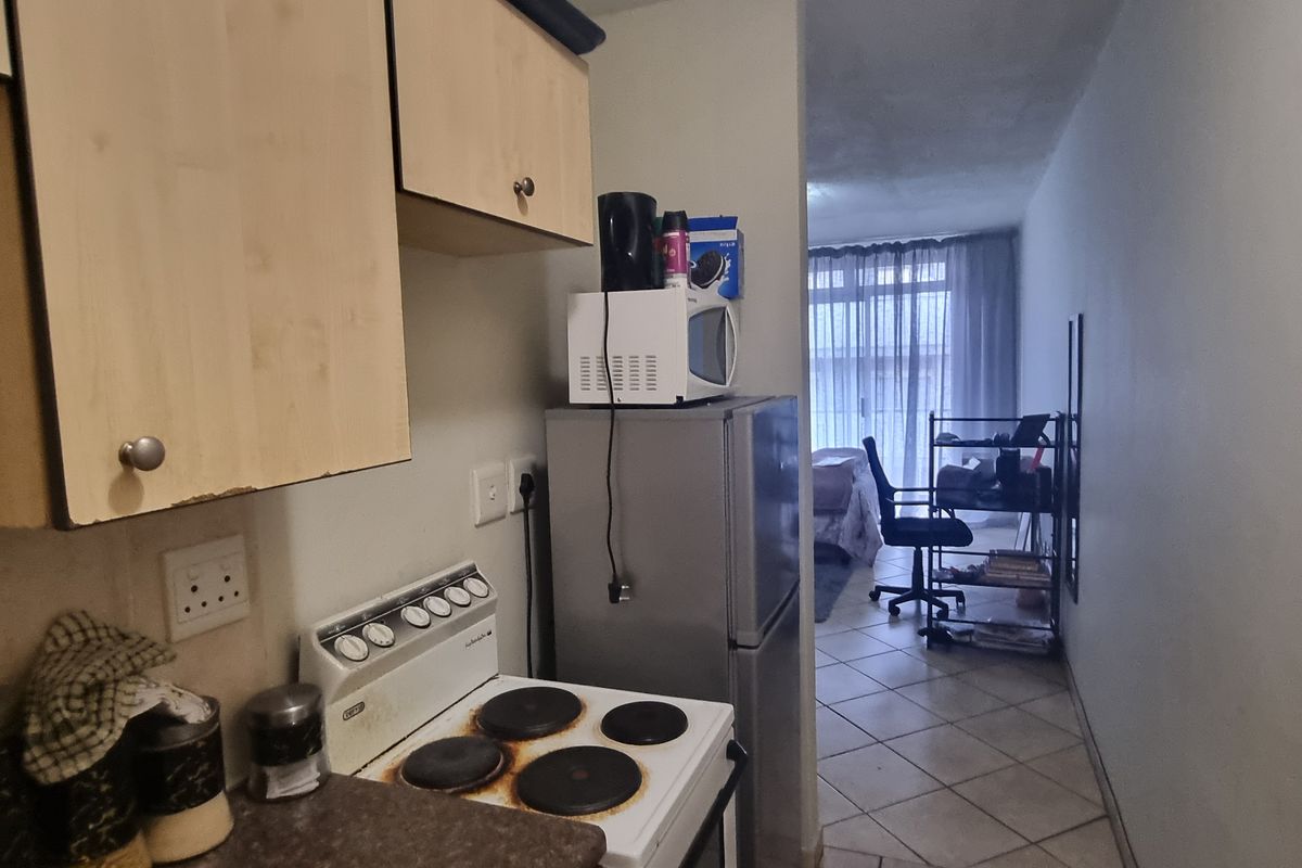 Compact kitchen featuring laminate cabinetry, an electric stove, and tiled flooring, leading into an adjacent living area.