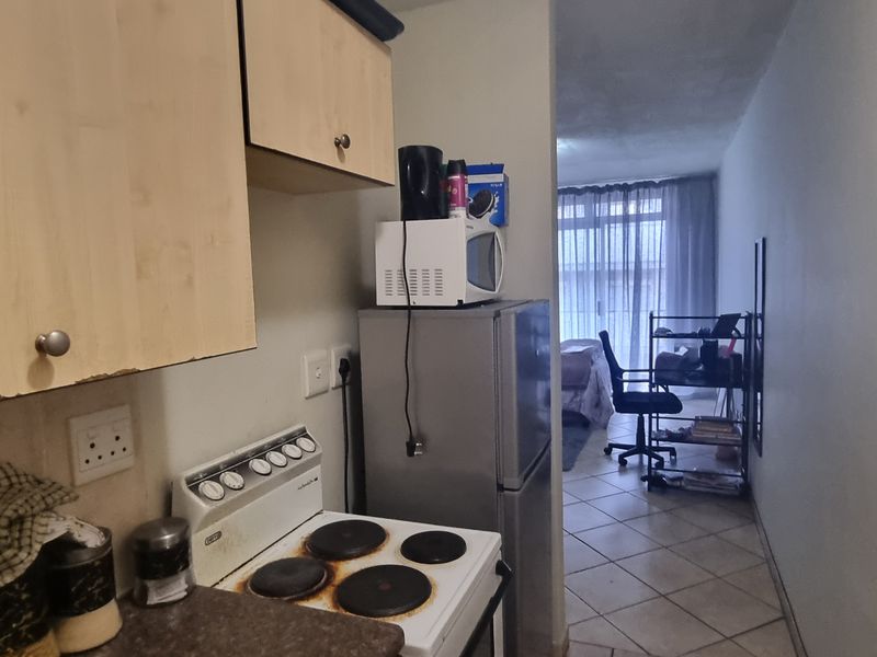 Compact kitchen featuring laminate cabinetry, an electric stove, and tiled flooring, leading into an adjacent living area.