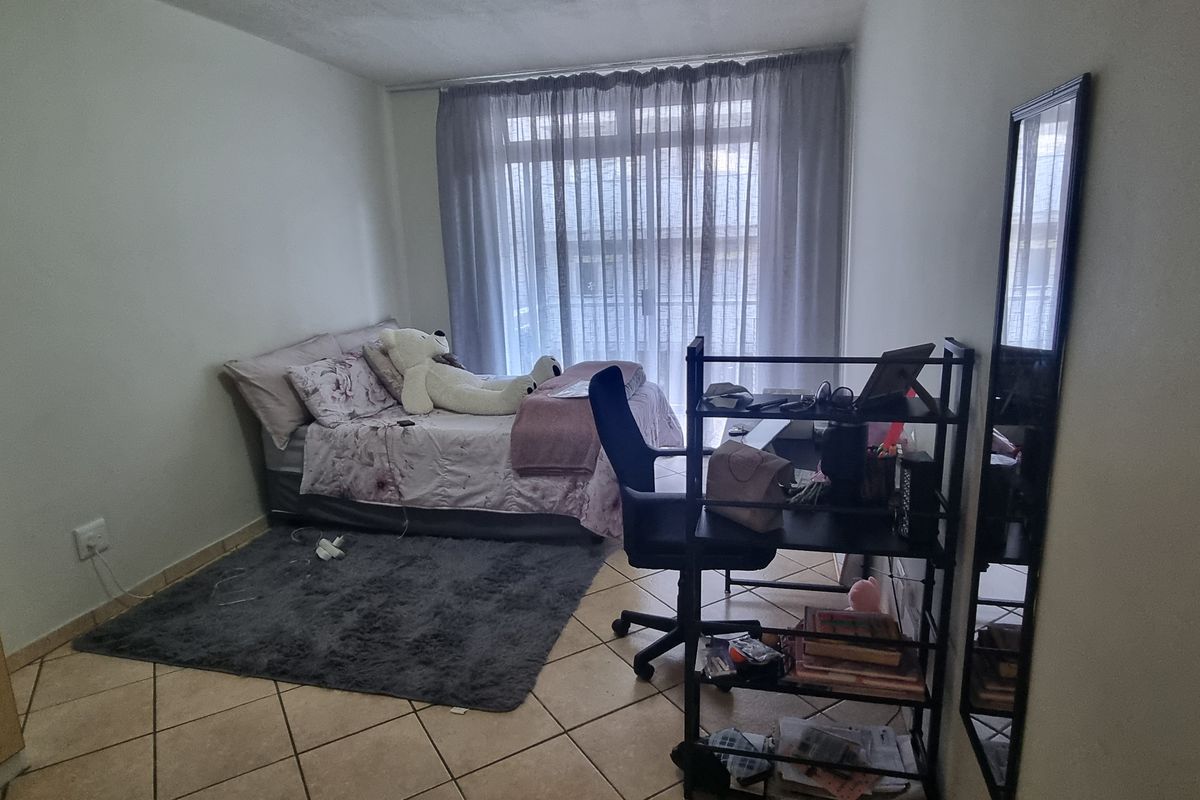 A functional bedroom featuring tiled flooring, a built-in wardrobe, and a sliding glass door providing access to the exterior.