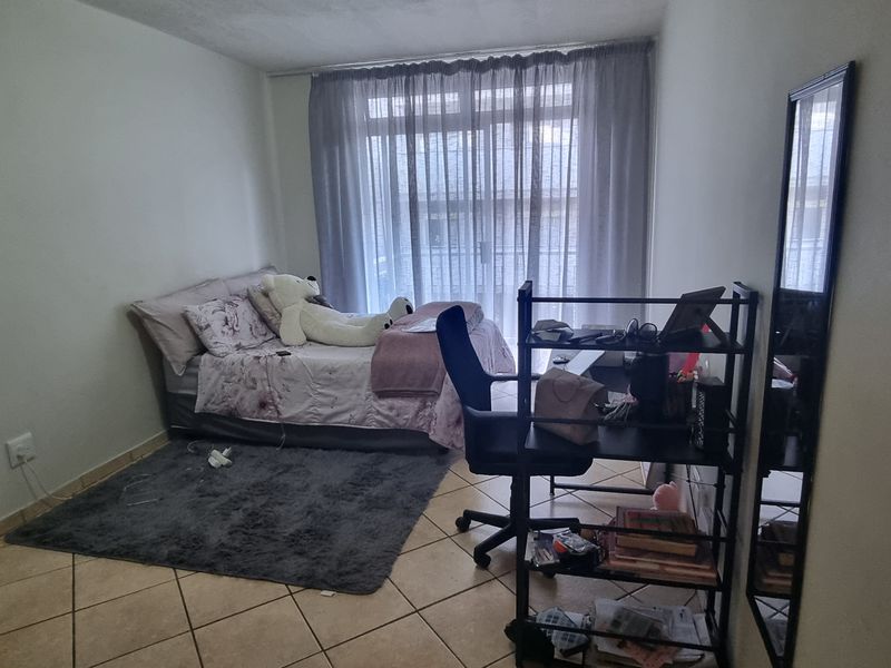 A functional bedroom featuring tiled flooring, a built-in wardrobe, and a sliding glass door providing access to the exterior.