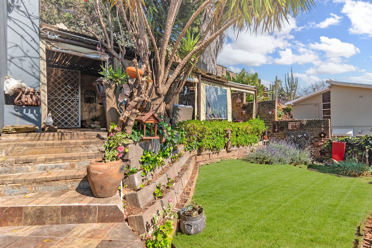 A well-maintained rear garden featuring a stone retaining wall, tiled staircase leading to a covered patio area, and established landscaping.