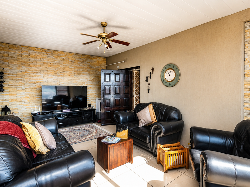 A comfortable living room featuring a textured stone accent wall, tiled flooring, and a timber-panelled ceiling with an integrated fan.