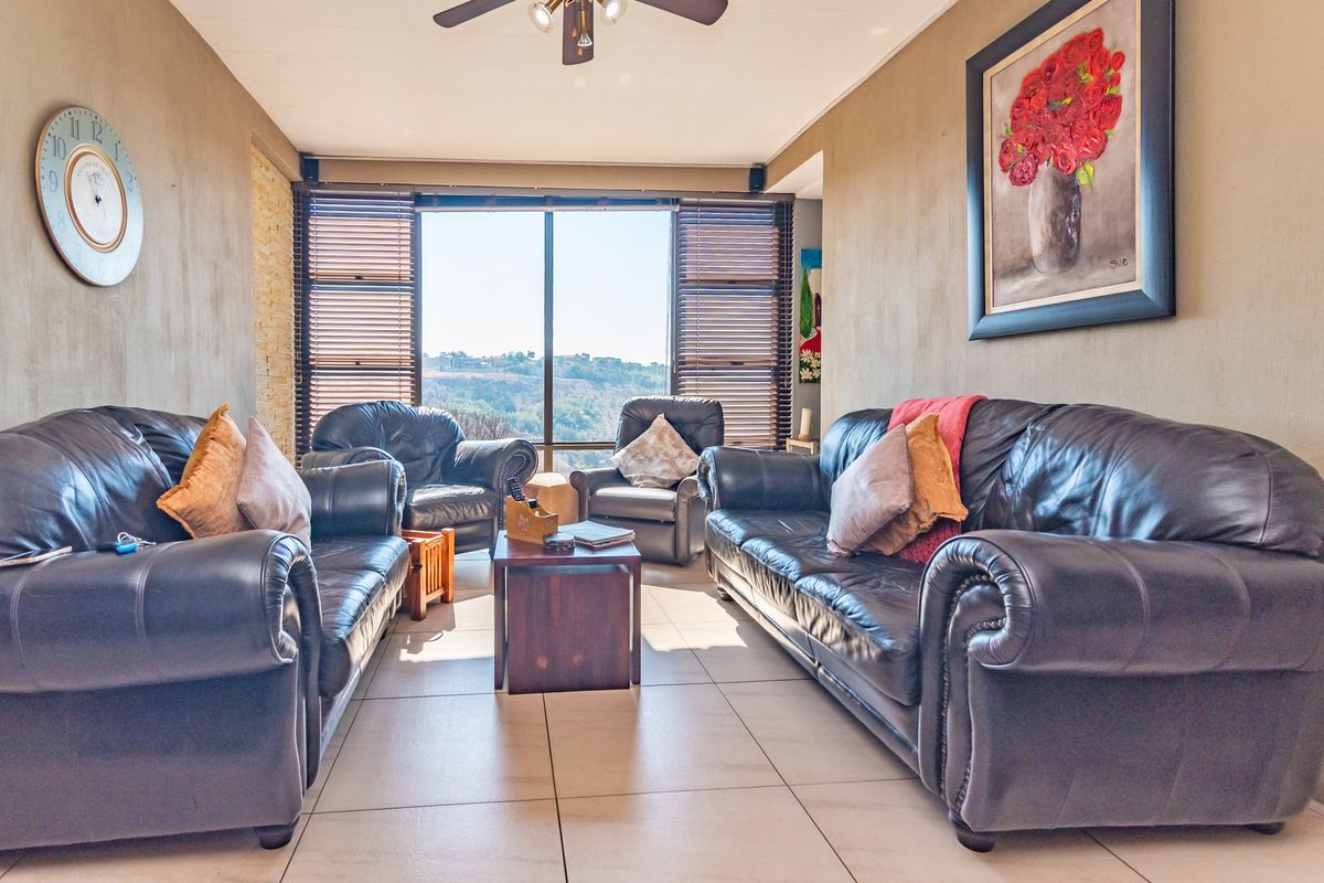 A comfortable living room featuring tiled flooring, a ceiling fan, and a large window with venetian blinds offering scenic views.
