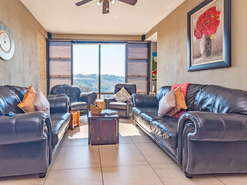 A comfortable living room featuring tiled flooring, a ceiling fan, and a large window with venetian blinds offering scenic views.