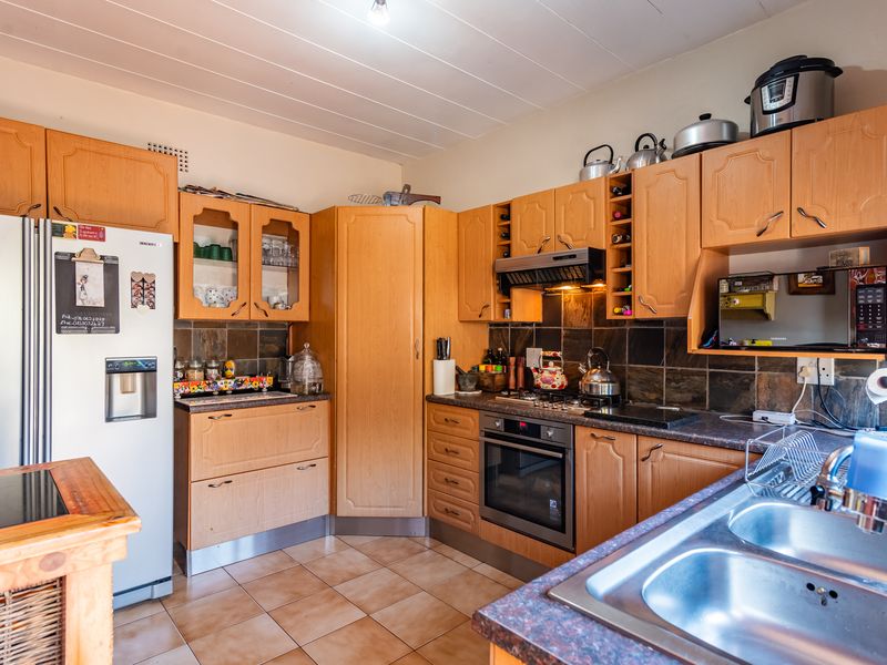 A functional kitchen featuring wood-tone cabinetry, tiled splashbacks, built-in oven and hob, and a double stainless steel sink.