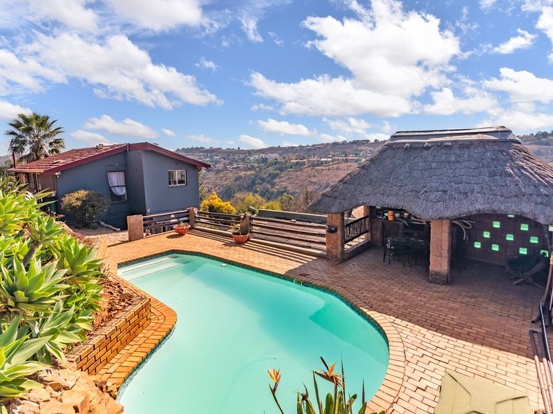 Outdoor entertainment area featuring a swimming pool and a traditional thatched lapa, set against a scenic hillside backdrop.