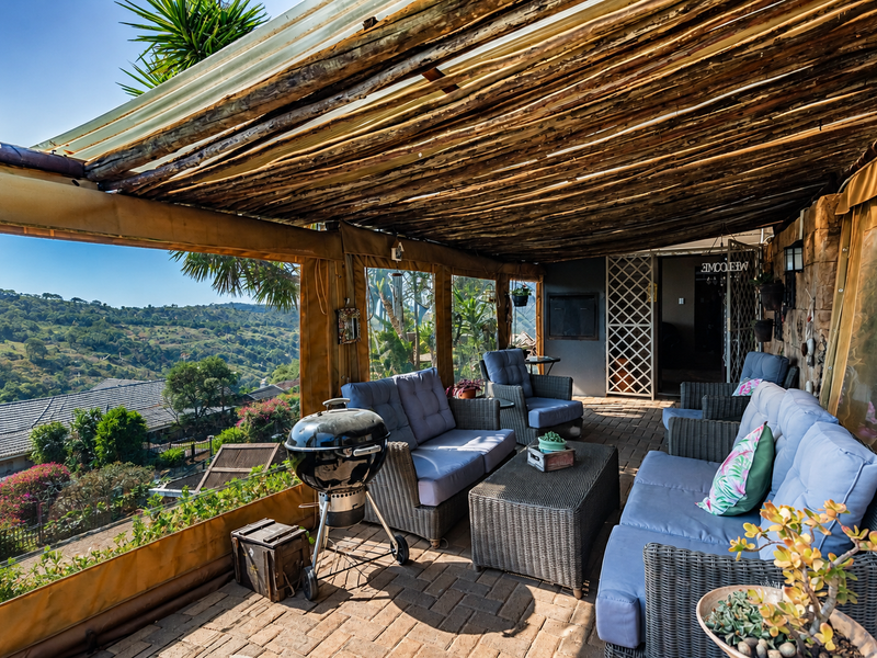 Covered outdoor patio featuring a rustic thatched roof, brick paving, and clear weather blinds, offering scenic elevated views of the surrounding landscape.
