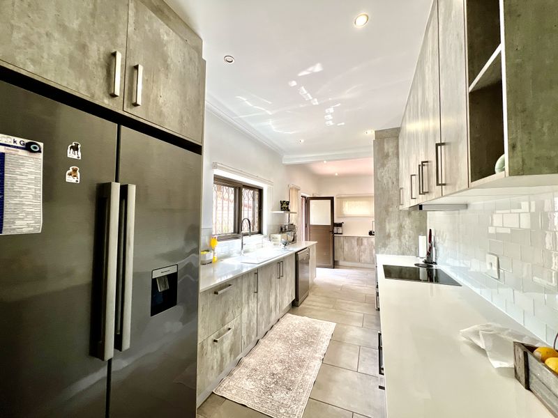 Modern galley-style kitchen featuring contemporary concrete-look cabinetry, stone countertops, subway tile backsplash, and integrated cooking appliances with recessed lighting.