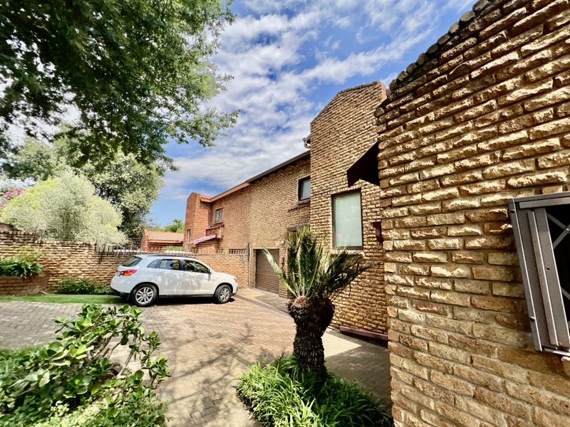 Front exterior view of the house featuring a textured brick facade, paved driveway, and established garden area.