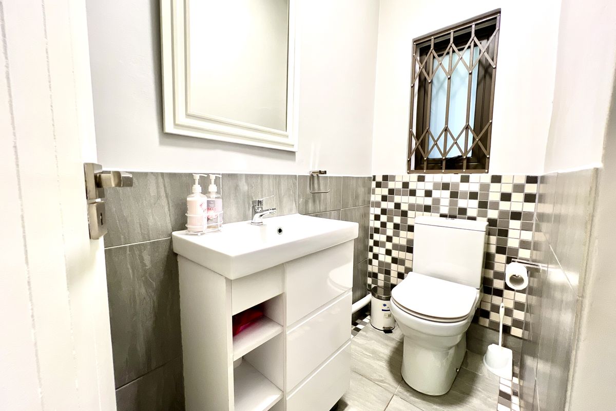 A modern, well-maintained bathroom featuring a sleek vanity cabinet, ceramic basin, toilet, and contemporary tiled finishes with a secure window.
