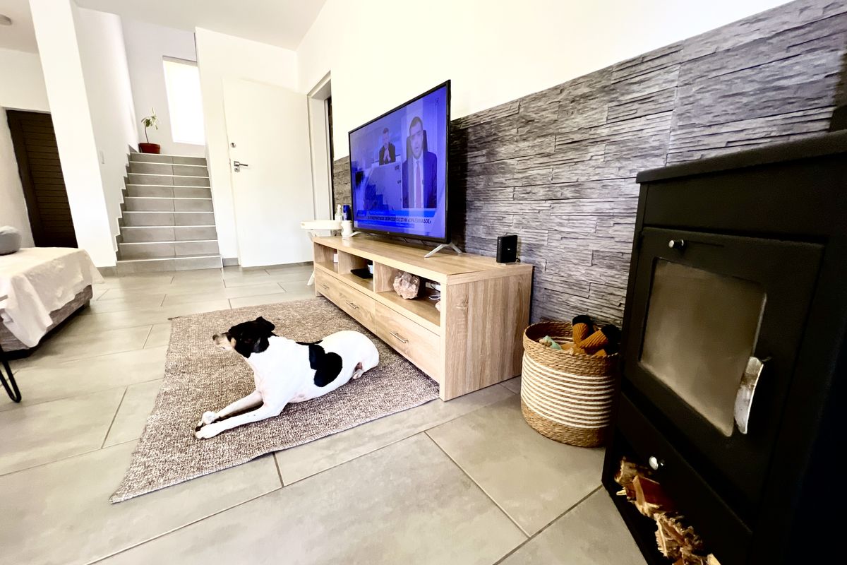 A modern living room featuring a stone-cladding accent wall, a built-in wood-burning stove, and tiled flooring, leading to an internal staircase.