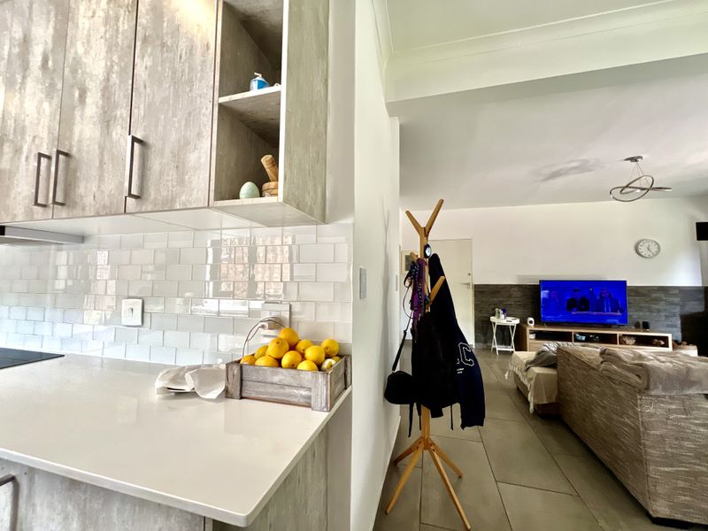 Open plan living area featuring a modern kitchen with subway tile backsplash and stone countertops, flowing into a spacious lounge with tiled flooring.