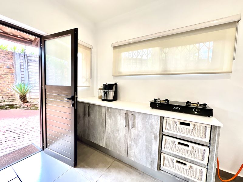 A modern scullery or prep area featuring grey wood-look cabinetry, stone countertops, and direct access to an outdoor patio area.