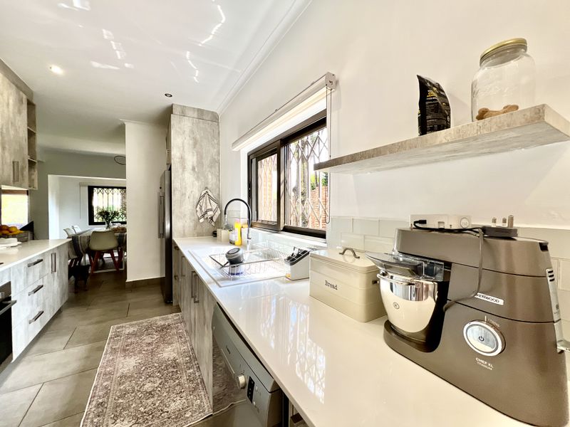 Modern kitchen featuring stone countertops, subway tile backsplash, ample cabinetry, and tiled flooring, with a view through to the adjacent dining area.