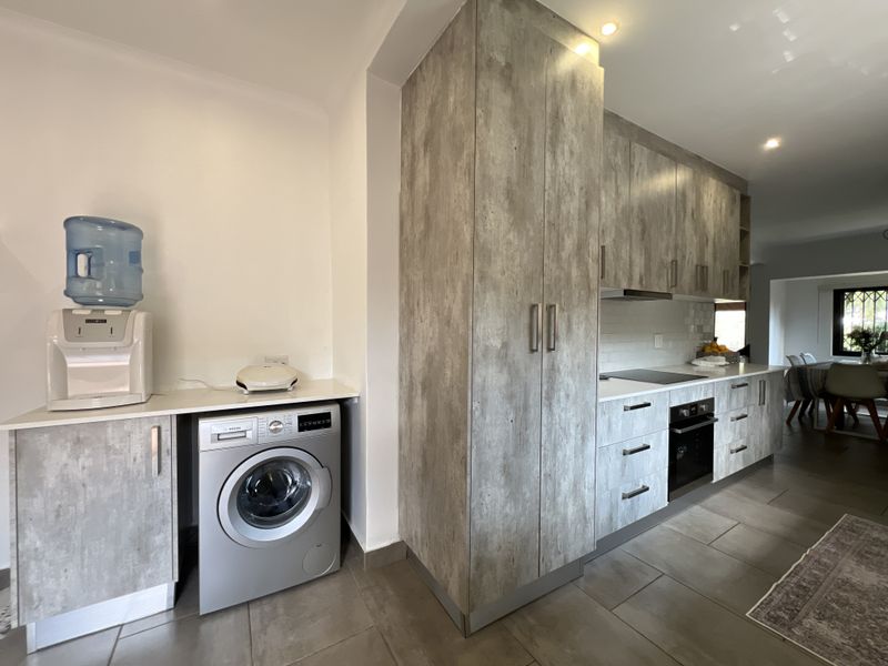 Modern kitchen featuring wood-look cabinetry, stone countertops, integrated oven, hob, and dedicated space for laundry appliances with tiled flooring throughout.