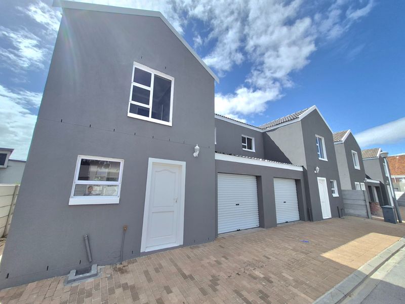 Front elevation of a modern townhouse featuring a double garage with roller shutter doors and a paved driveway.