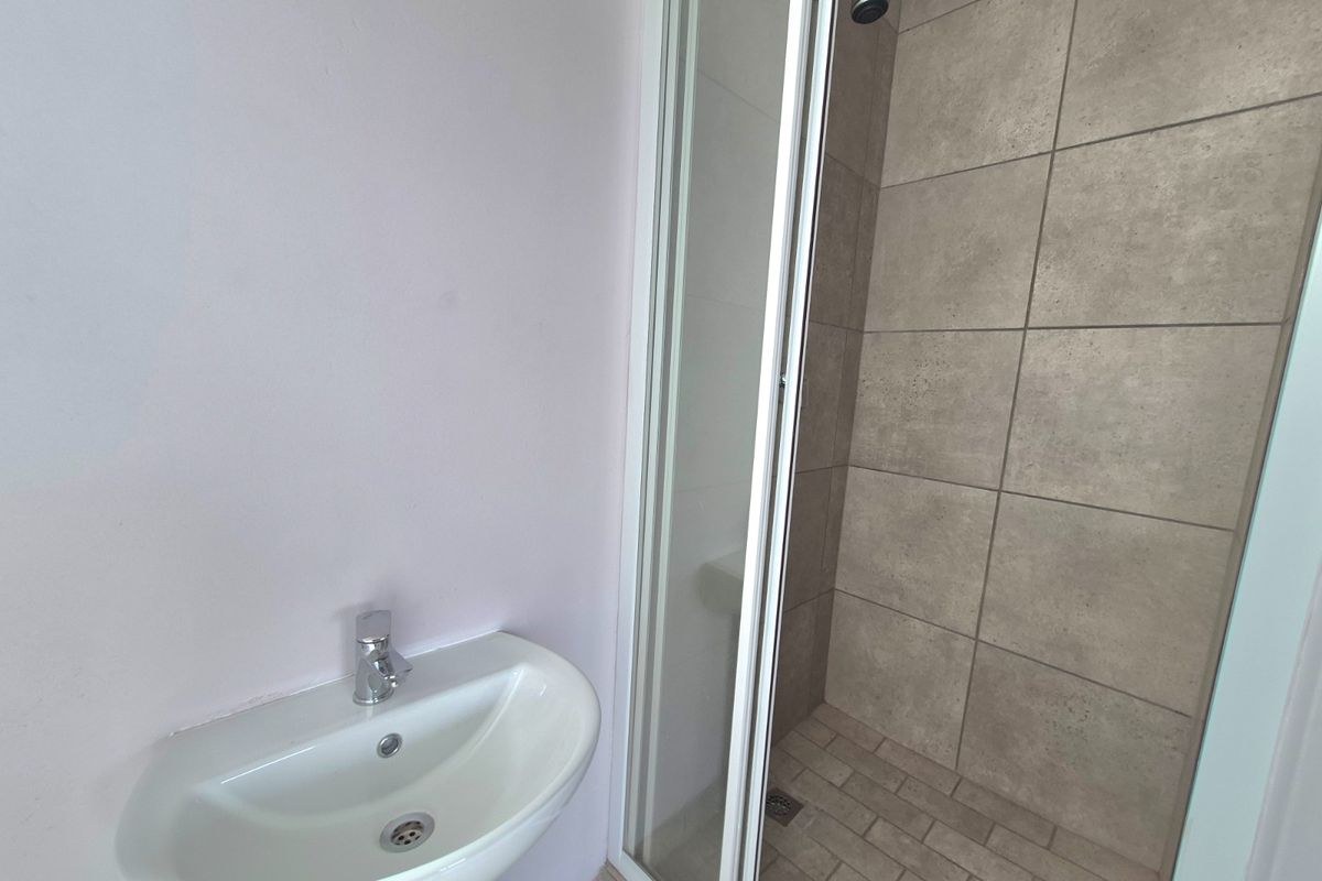 A clean, functional bathroom featuring a pedestal basin with a chrome mixer tap and a separate shower enclosure with tiled finishes.