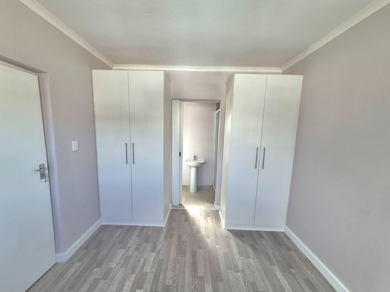 A clean, empty bedroom featuring built-in cupboards and laminate flooring, with an adjoining en-suite area containing a pedestal basin.