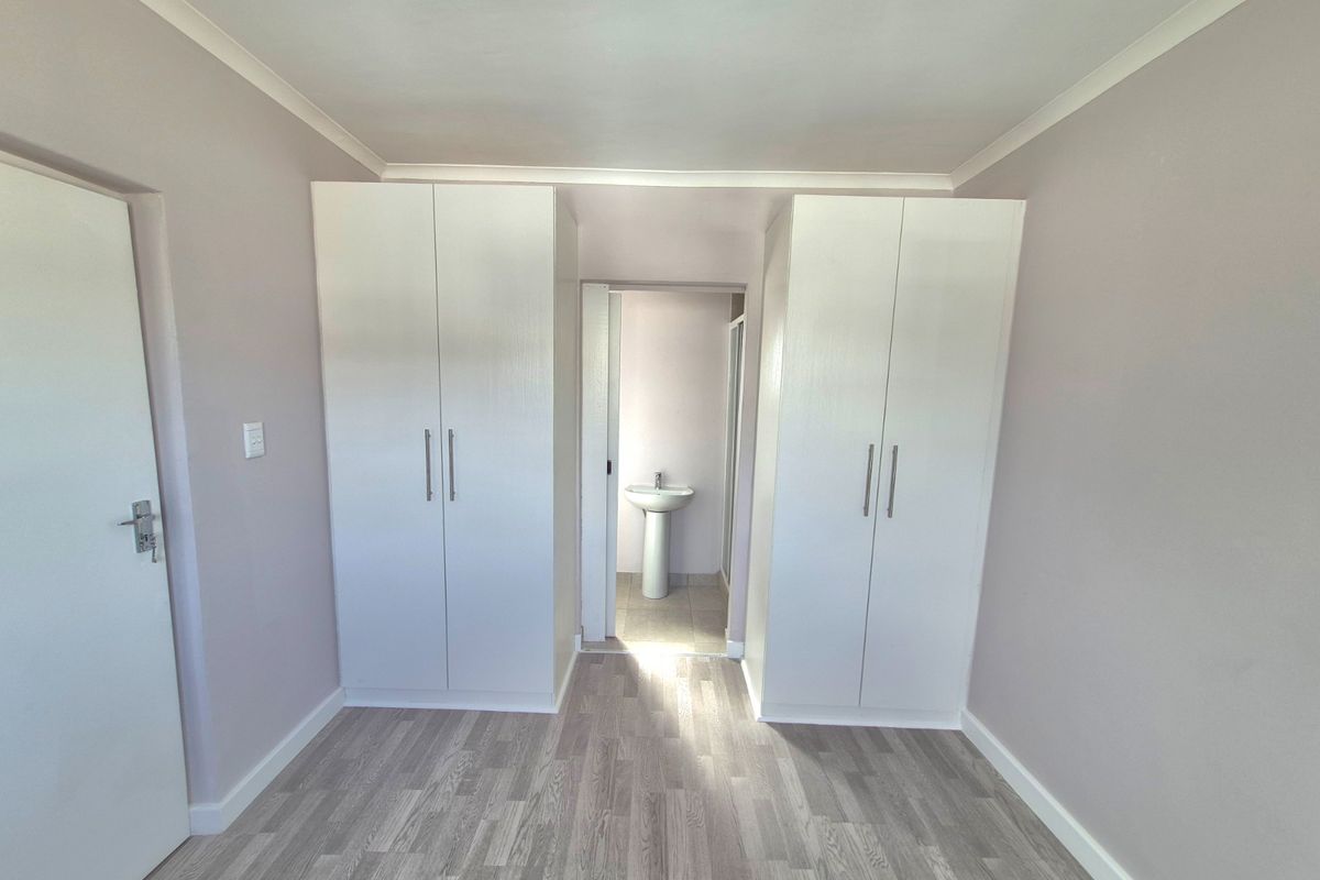 A clean, empty bedroom featuring built-in cupboards and laminate flooring, with an adjoining en-suite area containing a pedestal basin.