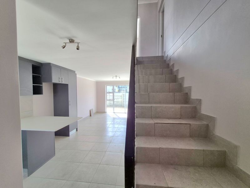 Open-plan living area featuring a tiled staircase with metal handrail, modern grey kitchen cabinetry with a peninsula, and direct access to the rear exterior.