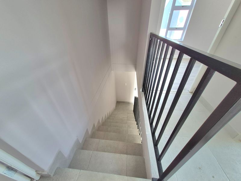 A bright, tiled staircase featuring a modern metal balustrade, providing a clean and functional transition between levels in the townhouse.