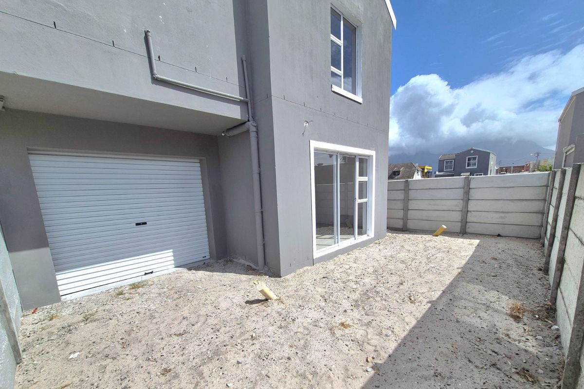 Rear exterior view of the townhouse featuring a roller garage door, sliding glass door access, and an unlandscaped backyard area enclosed by precast concrete walls.