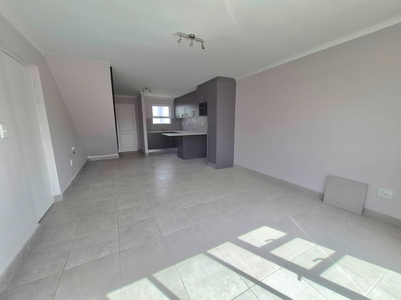 An open-plan living and kitchen area featuring neutral tiled flooring, modern grey cabinetry, and ample natural light.