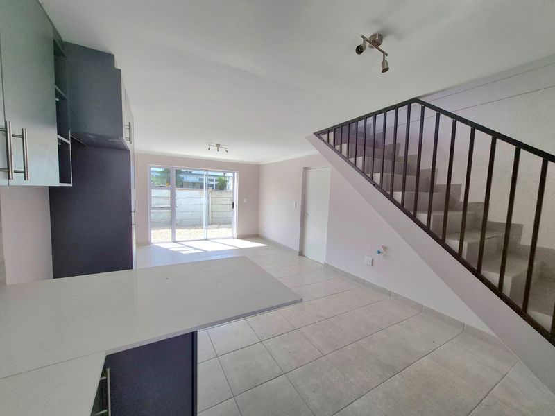 Open-plan living area featuring a modern kitchen with stone countertops, tiled flooring, and a staircase with a metal balustrade leading to the upper level.