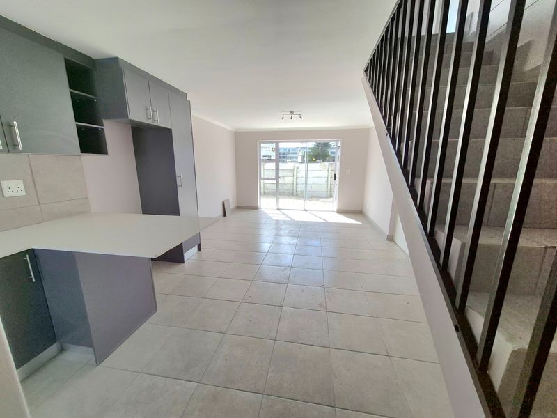 Open-plan living area featuring modern grey kitchen cabinetry, tiled flooring, and a staircase with a metal balustrade, leading to a rear sliding glass door.