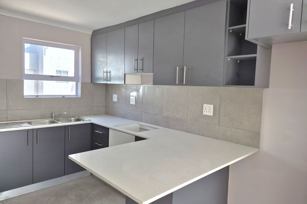 Modern kitchen featuring grey cabinetry, stone countertops, a breakfast nook, and a double basin sink with tiled backsplash.