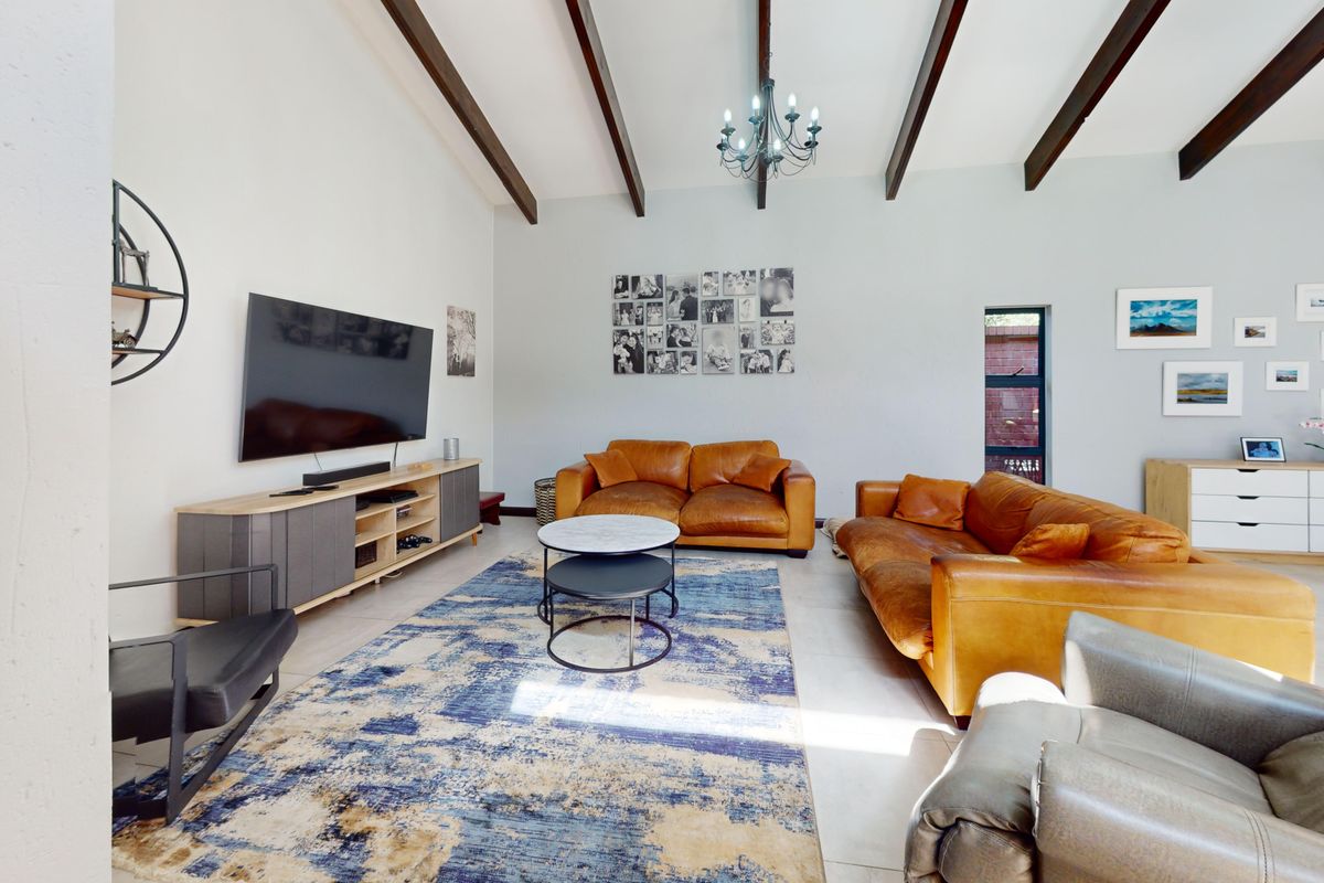 Spacious living room featuring high vaulted ceilings with exposed timber beams, tiled flooring, and a central chandelier.