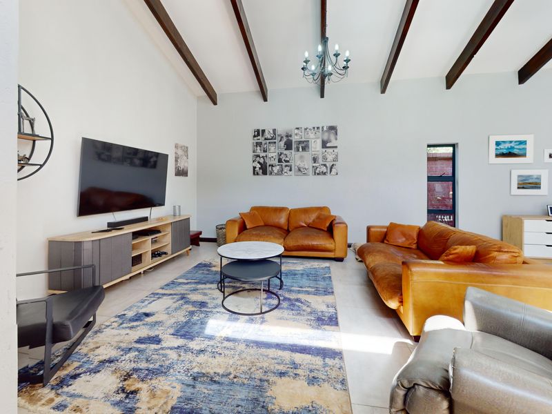 Spacious living room featuring high vaulted ceilings with exposed timber beams, tiled flooring, and a central chandelier.