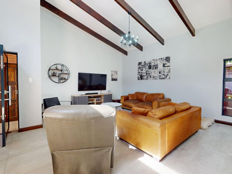 Spacious living room featuring a high vaulted ceiling with exposed timber beams, large format floor tiles, and natural light through an aluminium-framed window.