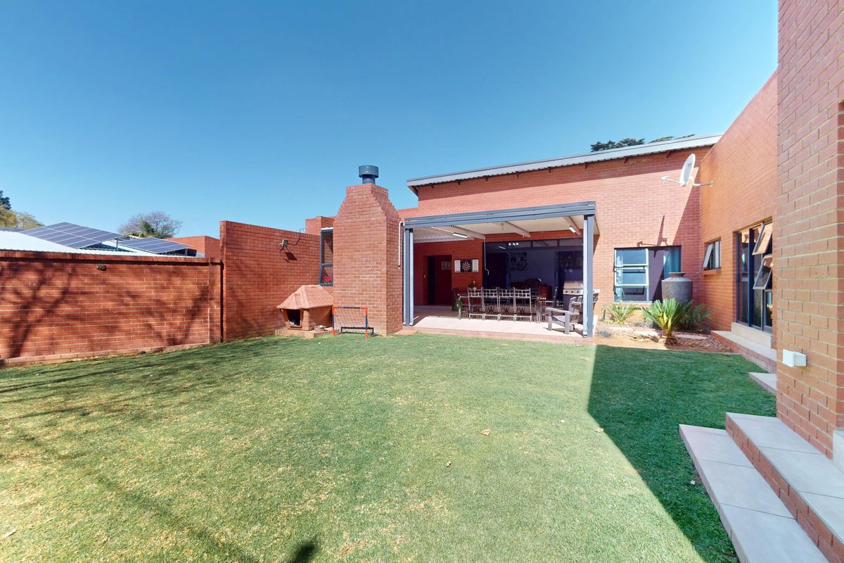 A well-maintained rear garden featuring a lawn, a covered patio area with a built-in brick fireplace, and brick boundary walls.