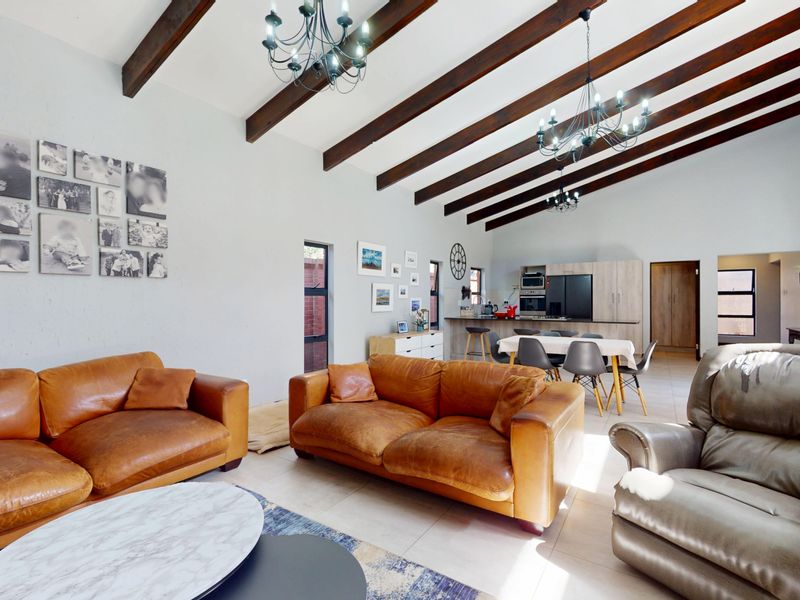 Spacious open-plan living and dining area featuring high vaulted ceilings with exposed timber beams, tiled floors, and a modern integrated kitchen.