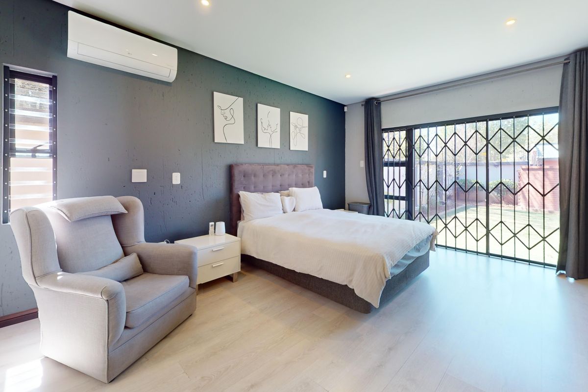 Spacious bedroom featuring laminate flooring, recessed lighting, a wall-mounted air conditioner, and large sliding doors with security gates leading to the garden.