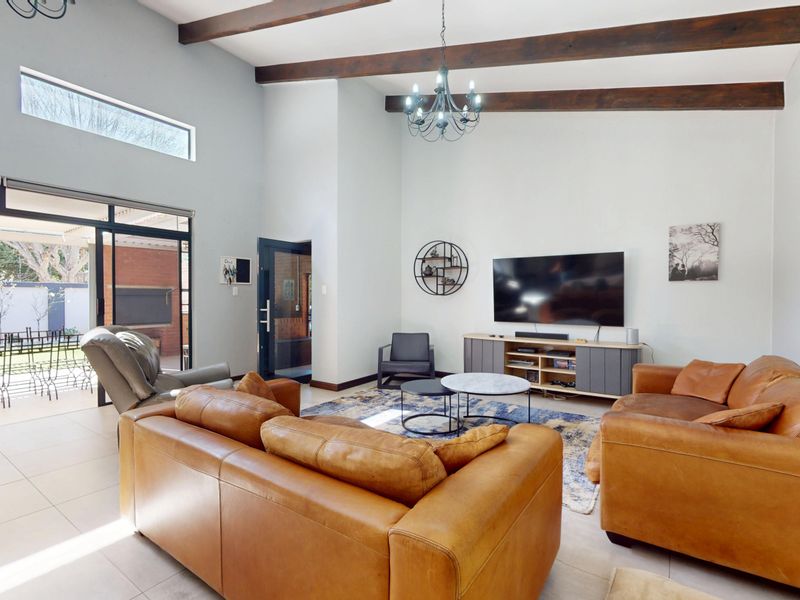 Spacious living room featuring high ceilings with exposed timber beams, tiled flooring, and large sliding glass doors providing seamless access to the outdoor patio area.