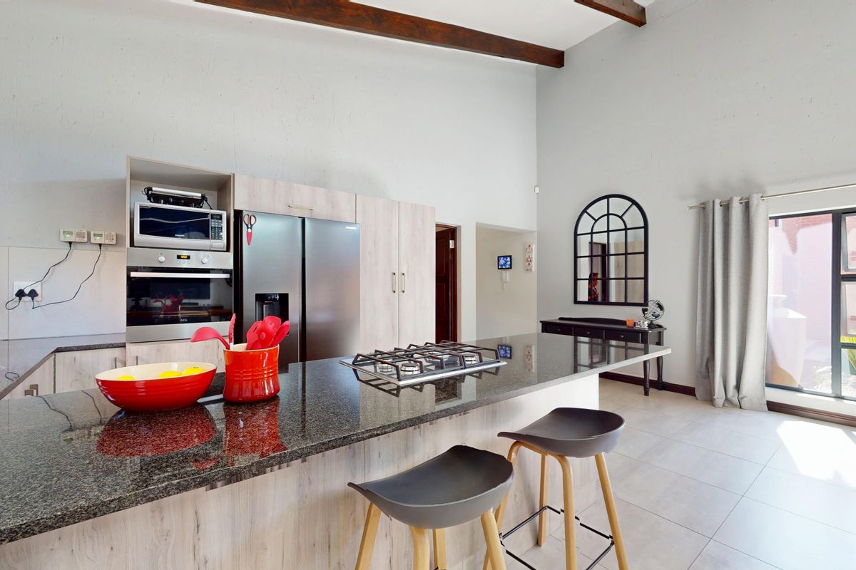 Modern kitchen featuring granite countertops, a central island with a gas hob, built-in appliances, and exposed timber ceiling beams.