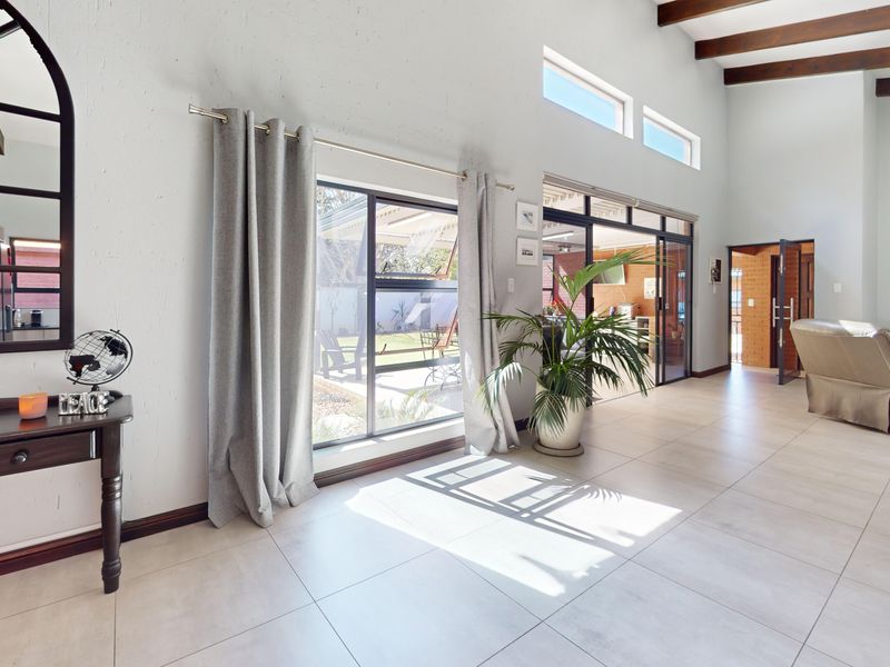 Spacious living area featuring high ceilings with exposed timber beams, large sliding glass doors providing natural light, and neutral tiled flooring.