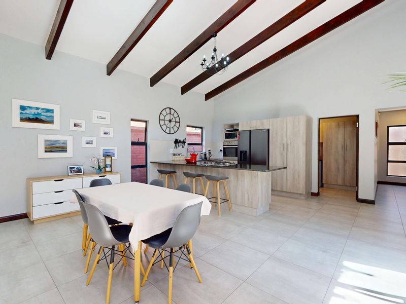 Spacious open-plan living and kitchen area featuring vaulted ceilings with exposed timber beams, modern cabinetry, and a central kitchen island with breakfast bar seating.