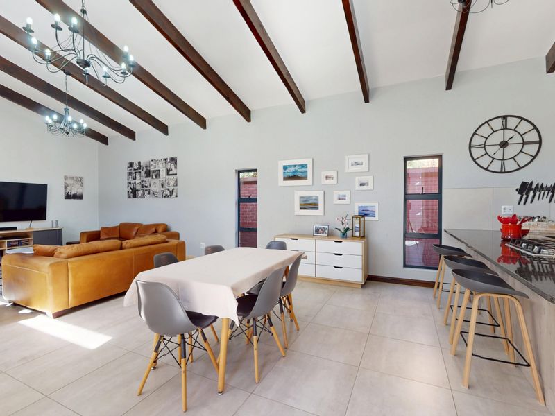Spacious open-plan living, dining, and kitchen area featuring high vaulted ceilings with exposed timber beams, tiled floors, and a modern kitchen with granite countertops.